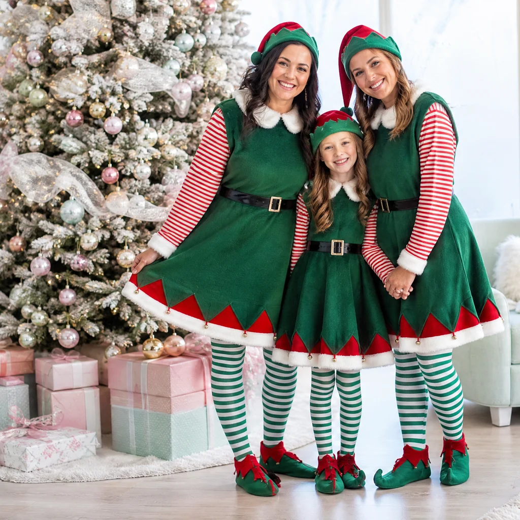 Three family members in Christmas elf outfits standing beside presents and a decorated tree