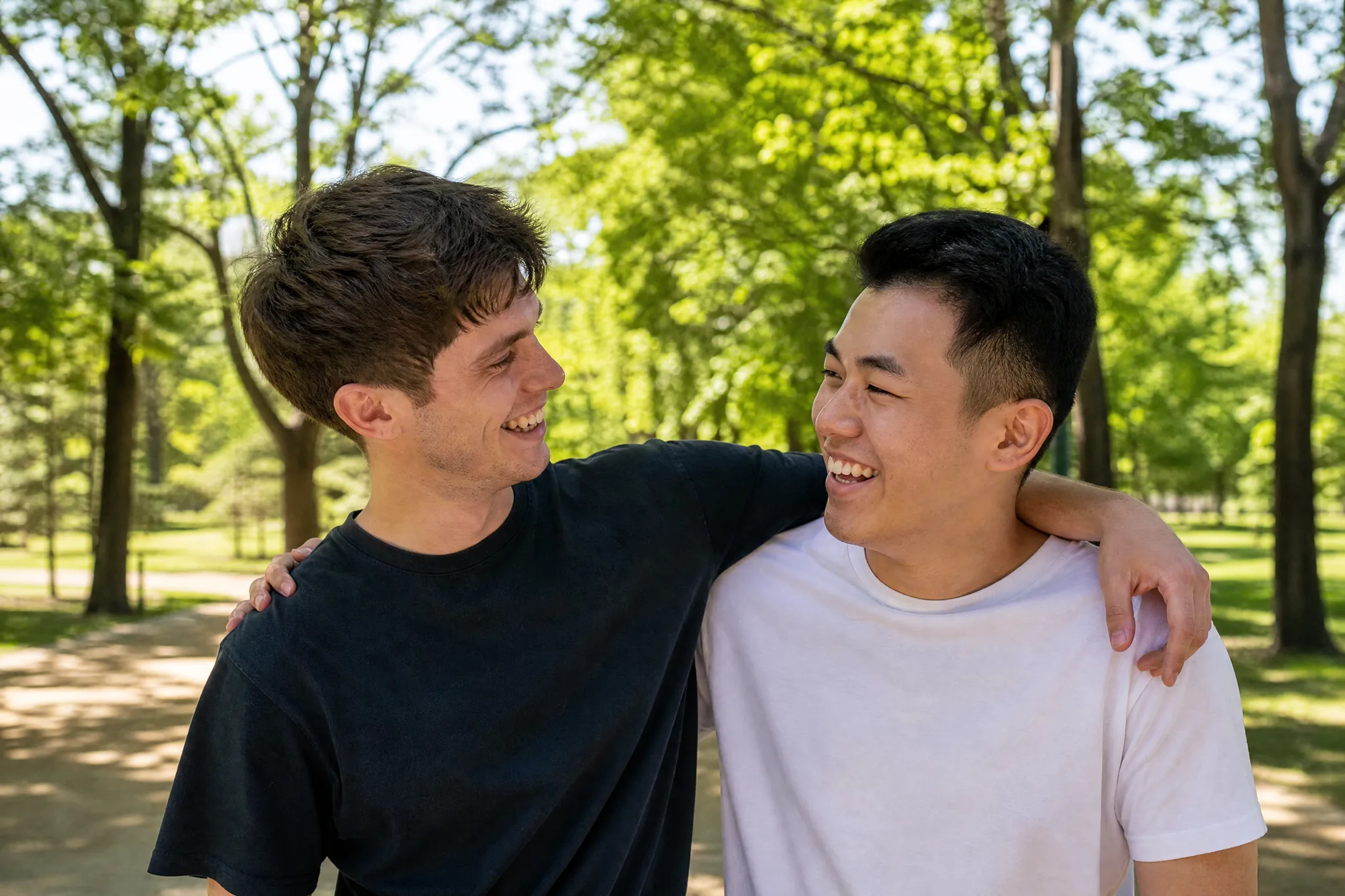AI Hugging Video: Laughing After the Embrace Two young men laughing with hands on each other’s shoulders just after a hug on a sunny path under green trees