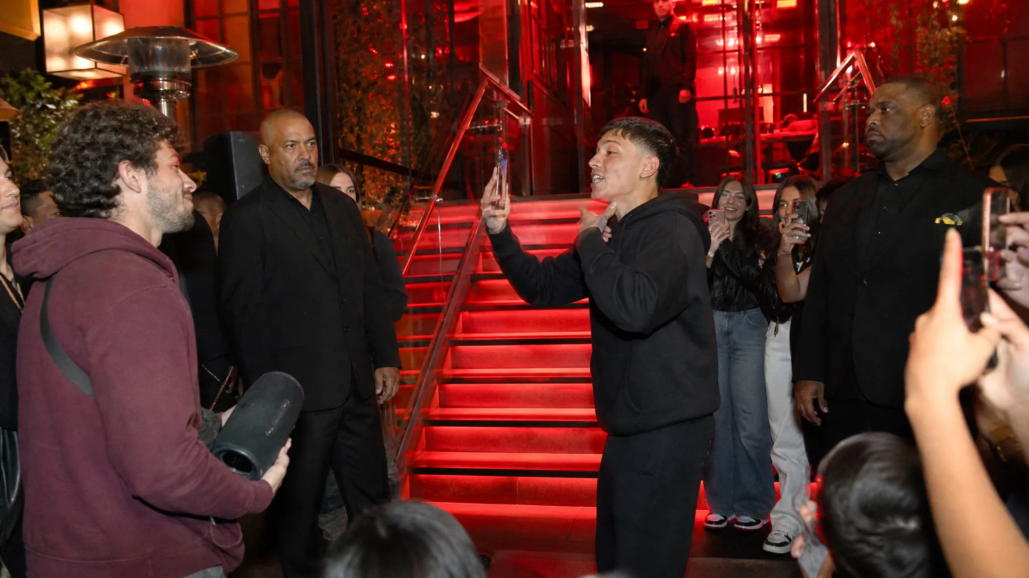 Bulin 47 AI Video Generator: Stairs, Speaker and Fans Wide night shot of red-lit stairs and glass railings, a rapper mid-verse, a man with a speaker and fans filming