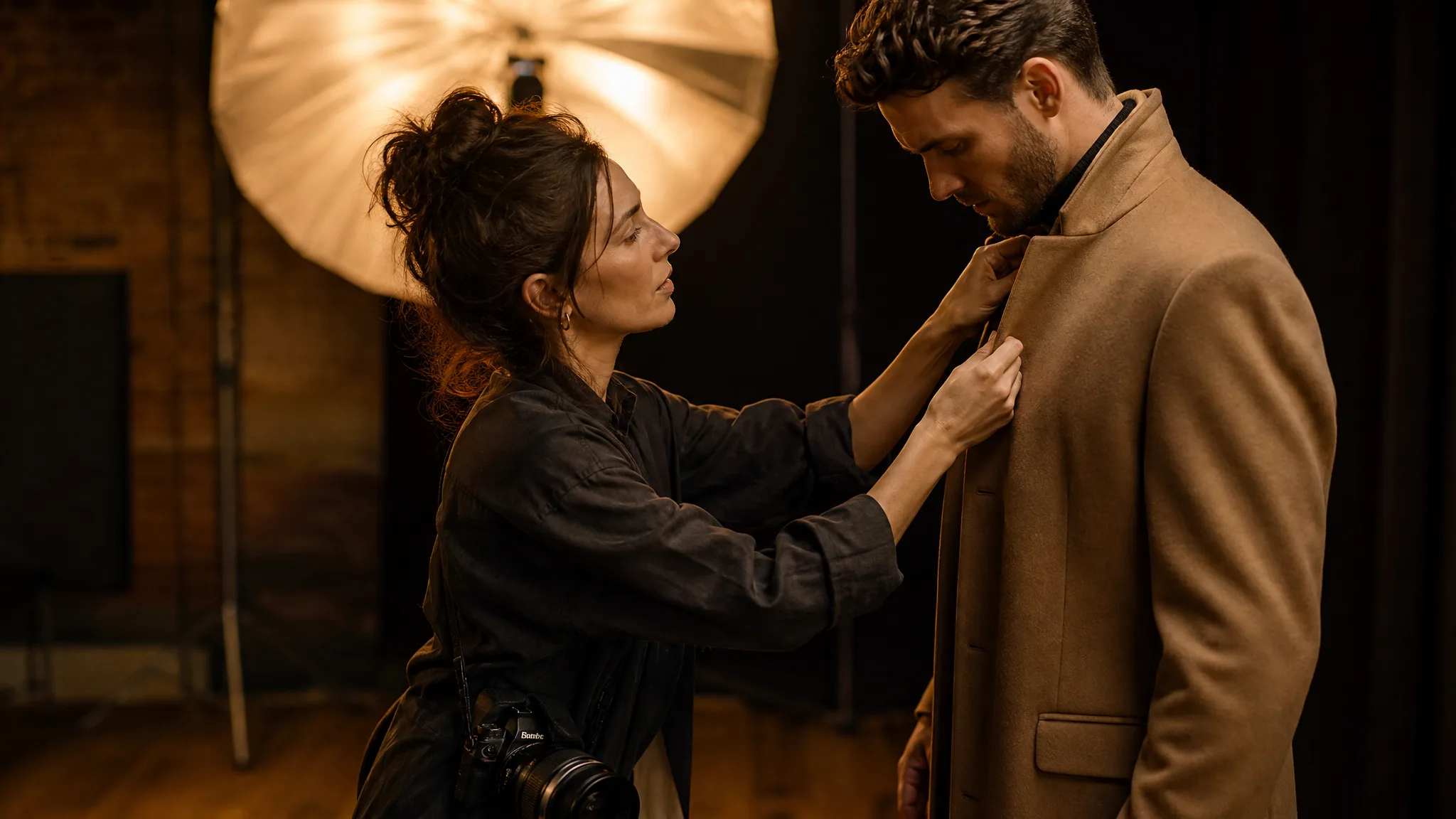 Fashion photographer straightening a model's coat collar in a warm studio