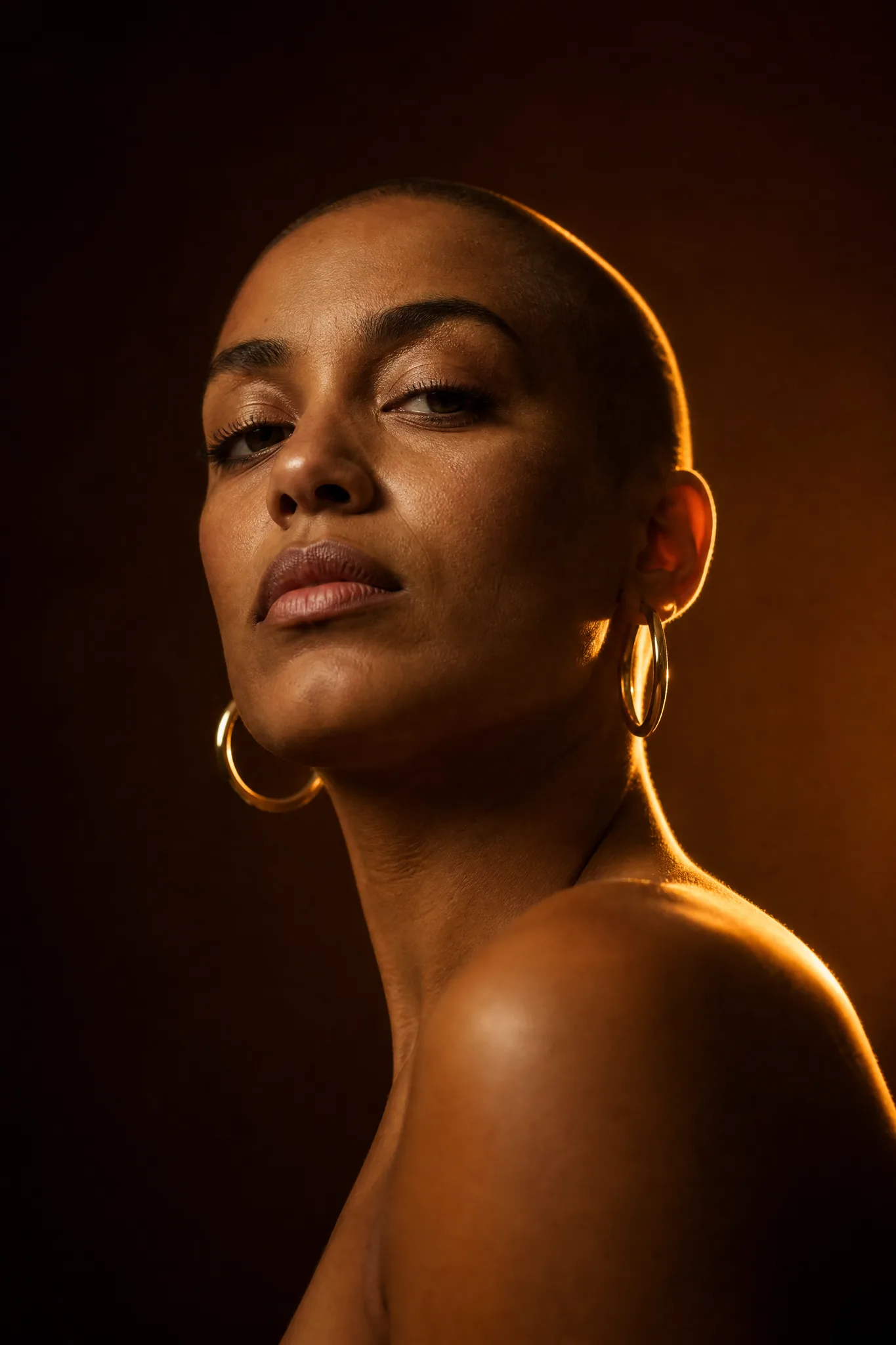 Grok Imagine Image: Rim-Lit Portrait Low-angle portrait of a woman with a shaved head and gold hoop earrings in warm backlight