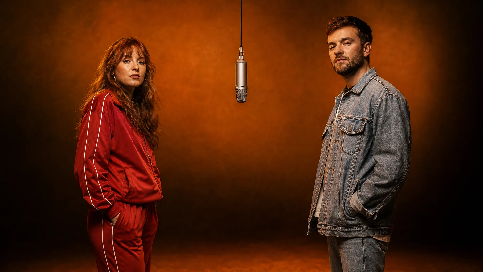 Left and Right Performers at One Mic Auburn-haired woman in a red tracksuit and a bearded man in a denim jacket on either side of a hanging silver mic