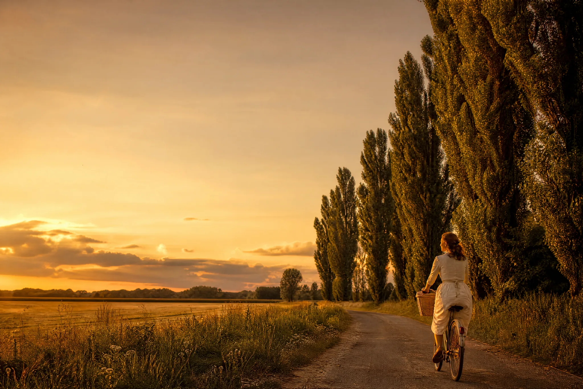 Nano Banana Pro: Country Lane with Open Sky Woman riding a vintage bicycle in the bottom corner of a country lane under a wide evening sky