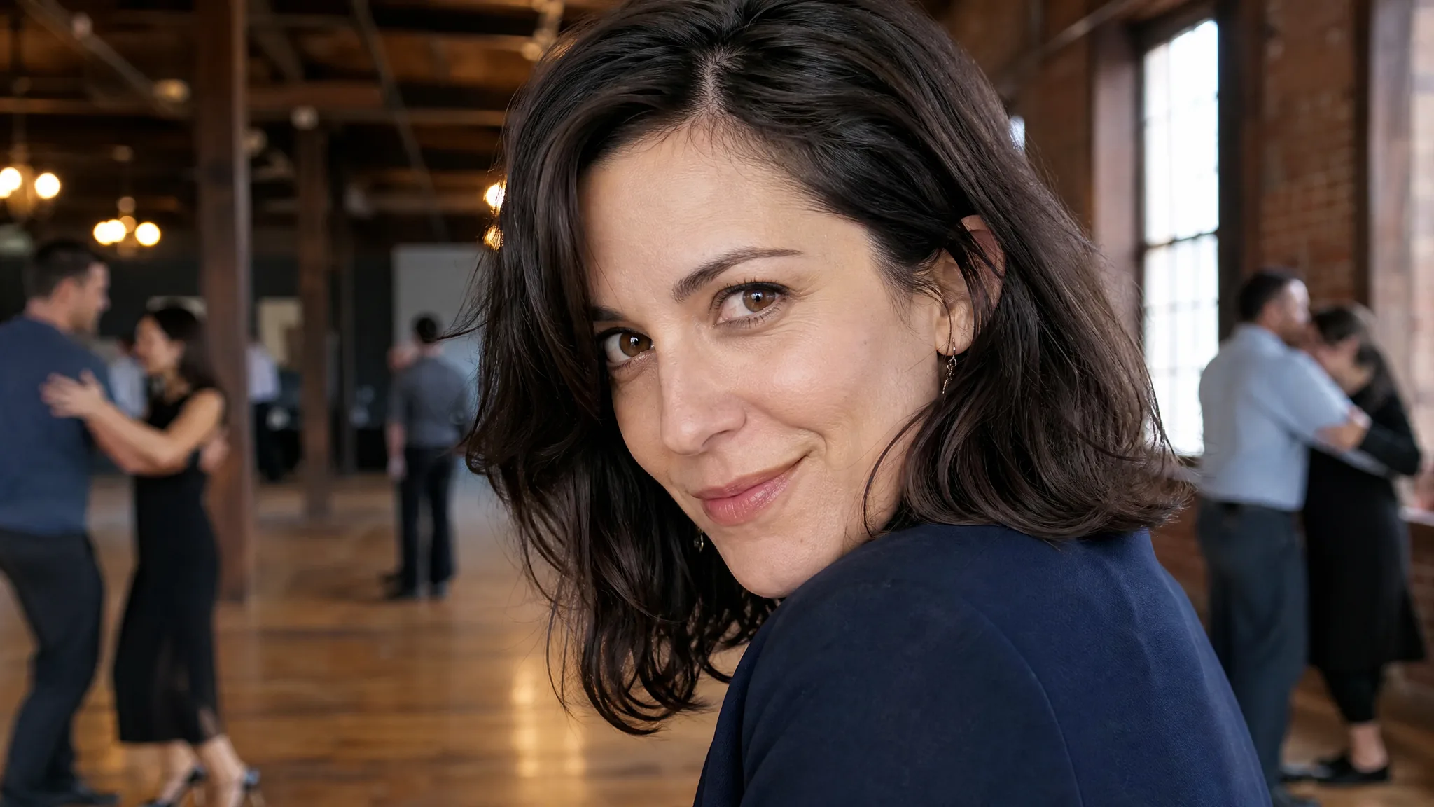 A dark-haired woman in a navy blazer smiling in a timber dance hall