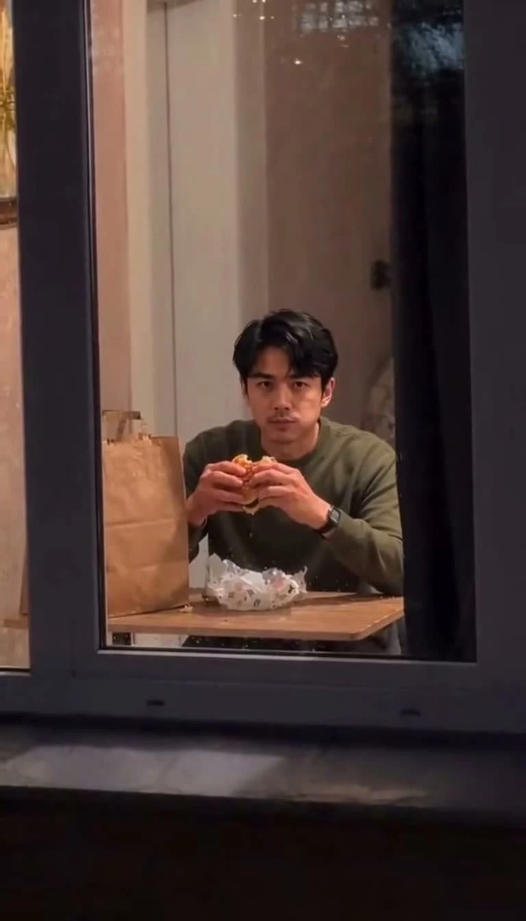 A character holding a burger while looking directly toward the window camera